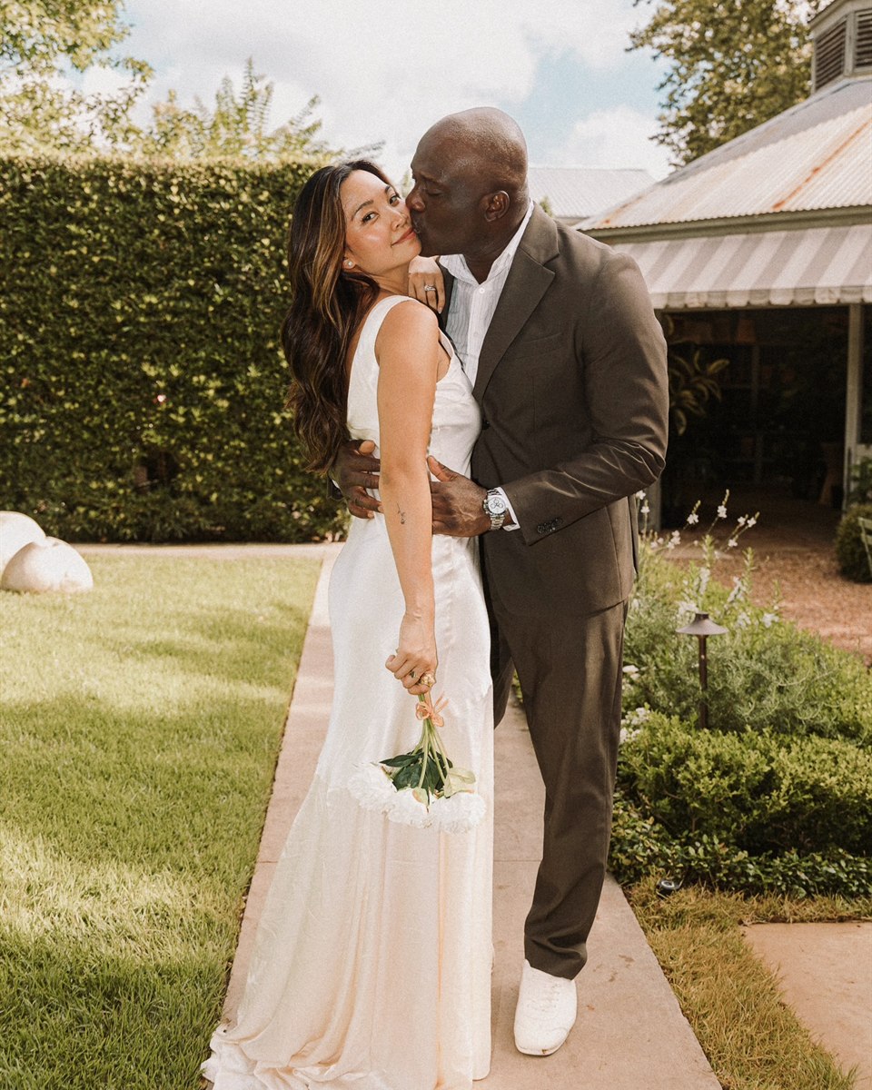 Nika and Emeka in full-length occasion looks in a sunlit garden.